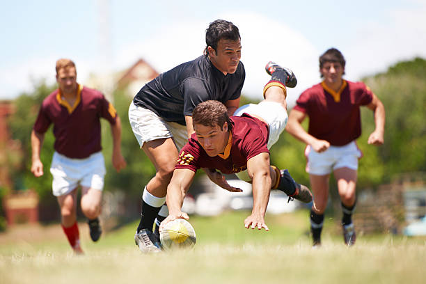 A rugby player dives to score a try while being chased by opponents.