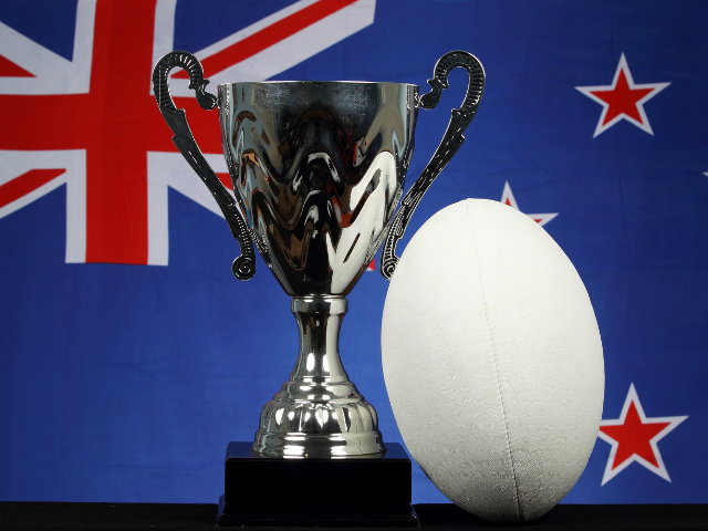 Trophy and rugby ball with New Zealand flag in the background.