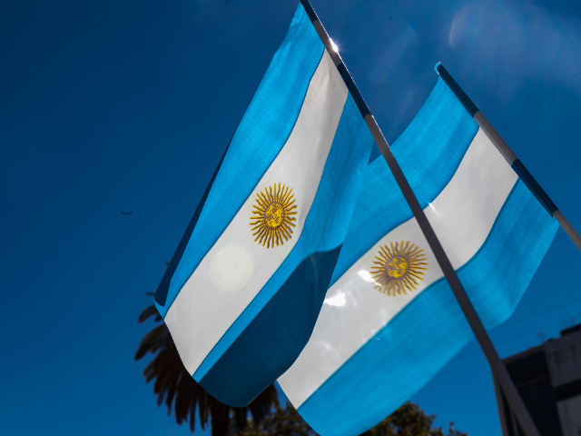 Two Argentina flags waving against a clear blue sky.