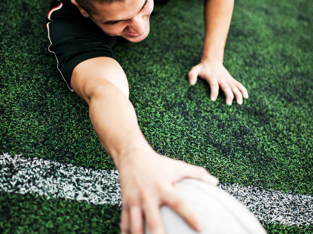 A rugby player reaching for the ball at the try line.