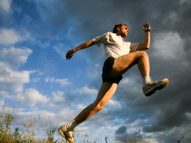 A man jumping high in an open field under a cloudy sky.