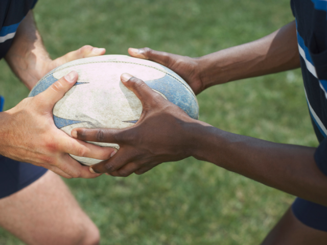 Two rugby players holding a rugby ball before a pass.