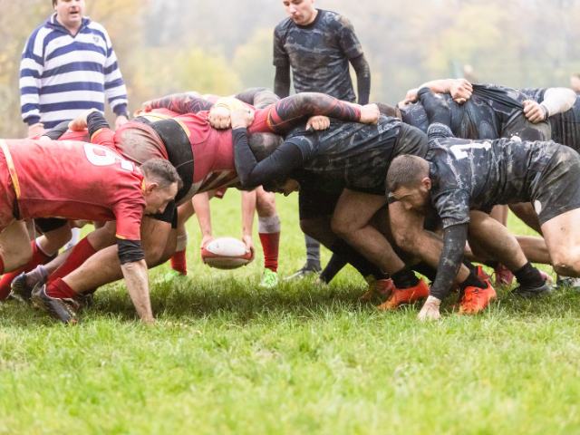 Rugby teams locked in a scrum on a grassy field.