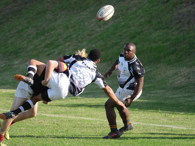 Rugby player passes the ball as two players tackle each other.