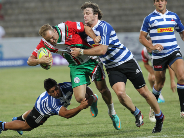 Rugby players in a hard tackle, one being brought down by two opponents.