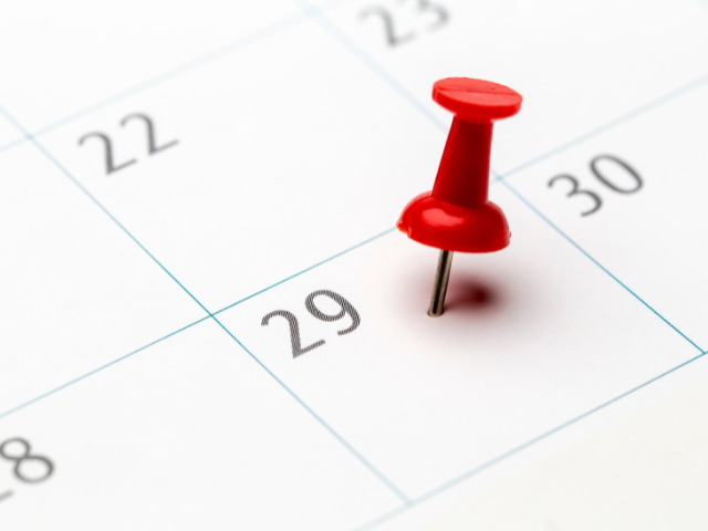 A close-up of a red pushpin placed on the 29th of a calendar.