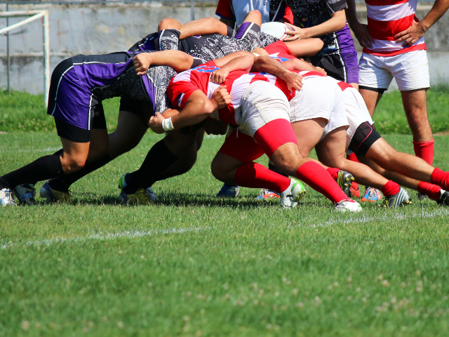 Rugby players engaging in a scrum during a match on a grassy field.