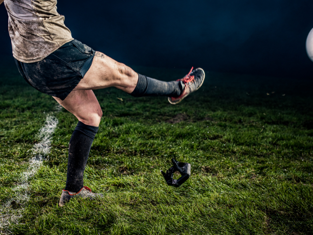 Rugby player kicking the ball on a muddy field during a night match.