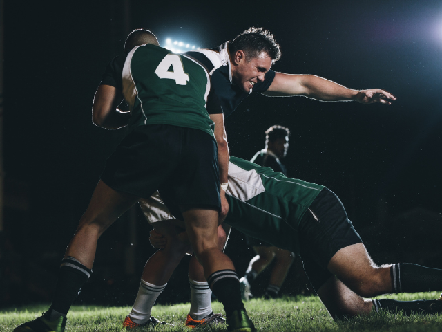 Rugby players in action, tackling an opponent during a nighttime match.