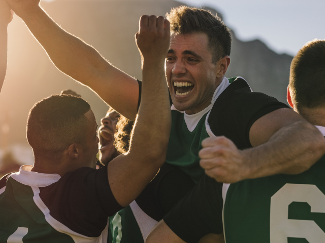 Rugby players celebrating a victory with arms raised in triumph.