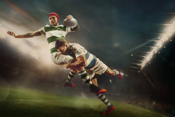 Rugby player being tackled mid-air while holding the ball during a night match.