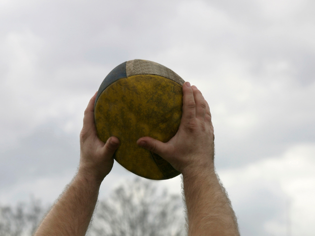 A close-up of hands holding a worn rugby ball above head, ready for a lineout.