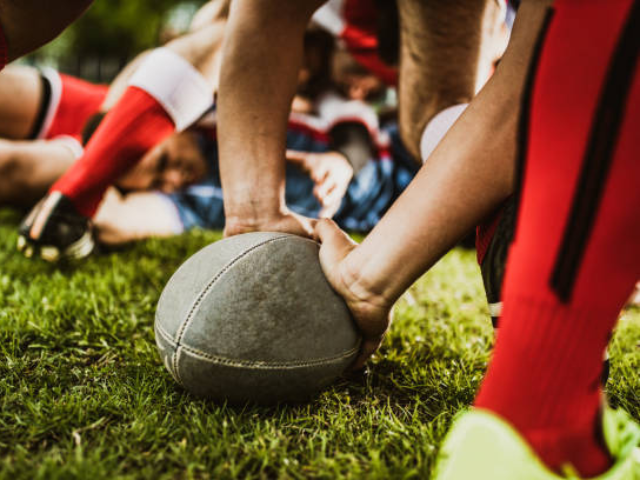 Close-up of rugby players engaged in a scrum with hands on the ball.