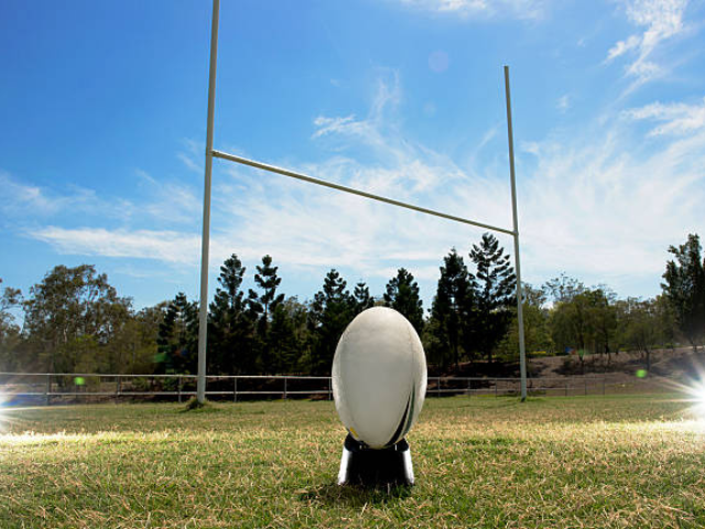 A rugby ball on a tee, ready for a kick toward the goalposts.