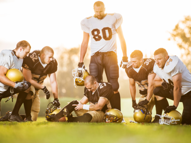 Football players surrounding an injured teammate during a game.