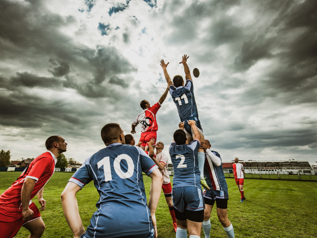 Rugby players competing for the ball during a line-out under a cloudy sky.