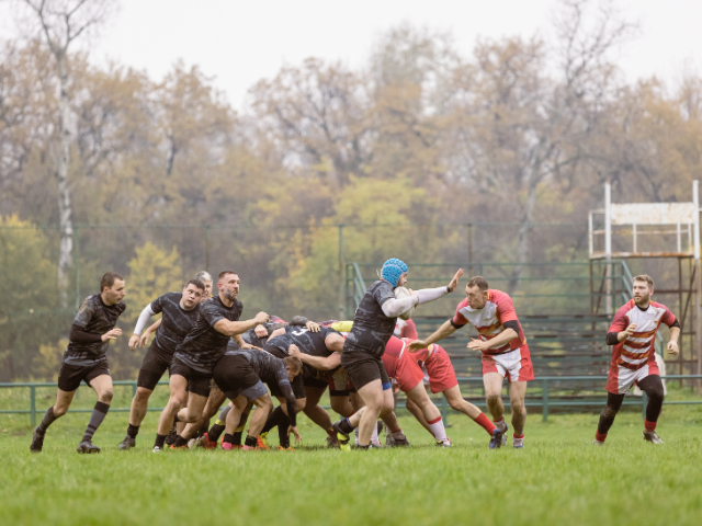 Teams competing in a wet and muddy rugby match on a grassy field.