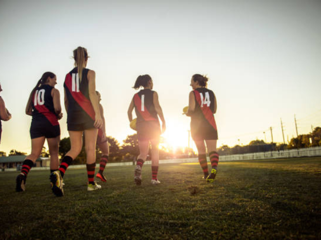 A women’s rugby team walking onto the field at sunset.