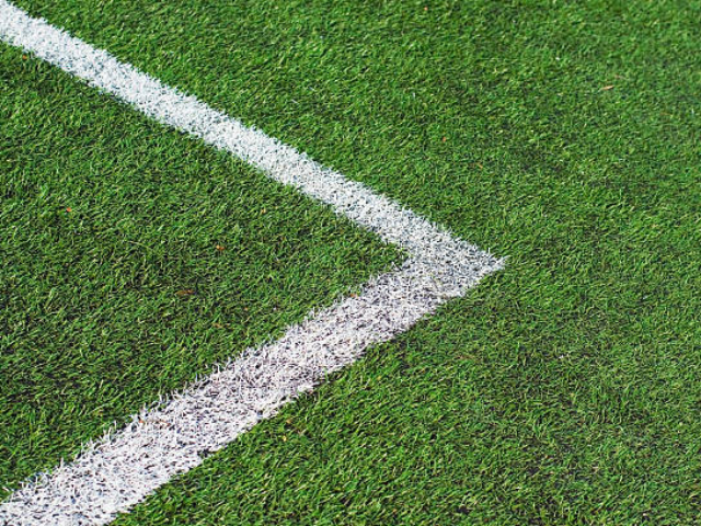 A close-up view of a white line marking the corner of a green sports field, with well-maintained grass.