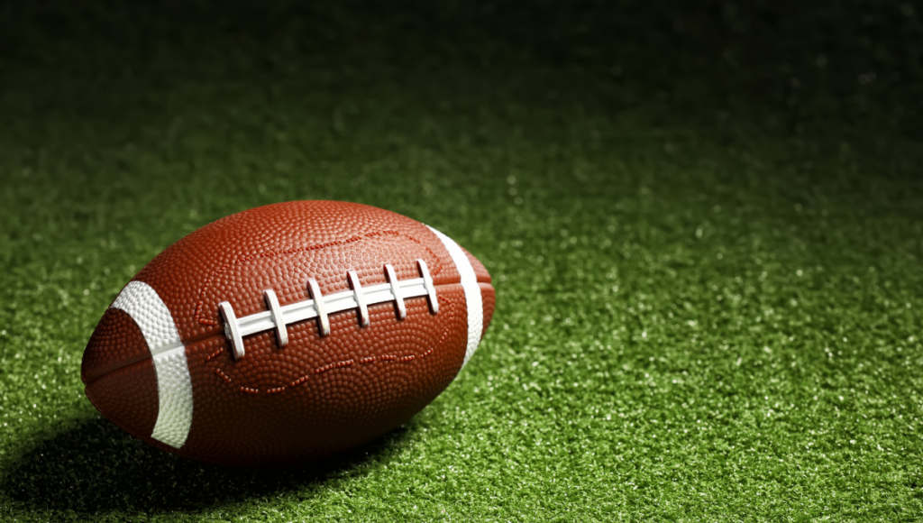 A close-up of a brown leather rugby ball sitting on green artificial turf.