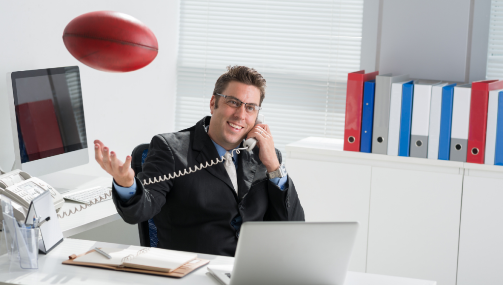 A businessman tossing a rugby ball in his office while on the phone.