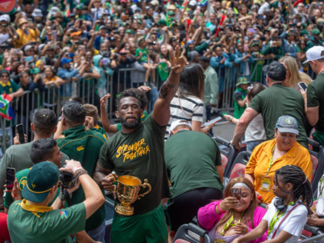 Siya Kolisi holding the Rugby World Cup trophy while celebrating with fans.