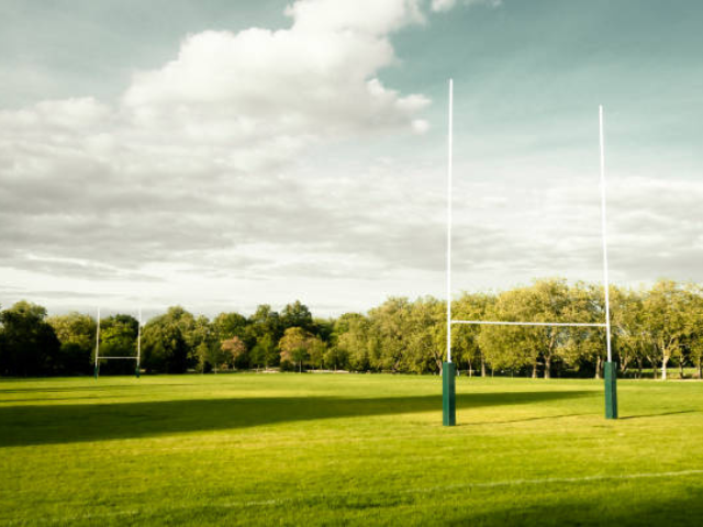 A peaceful, empty rugby field with goalposts and trees in the background.