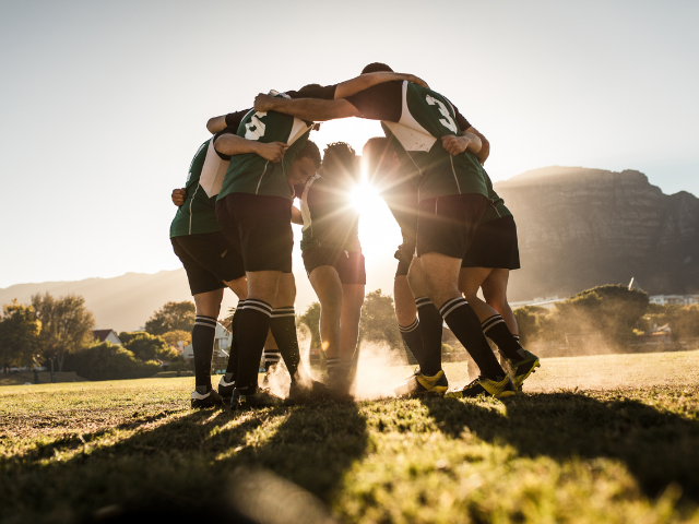 Rugby team huddle during sunset.