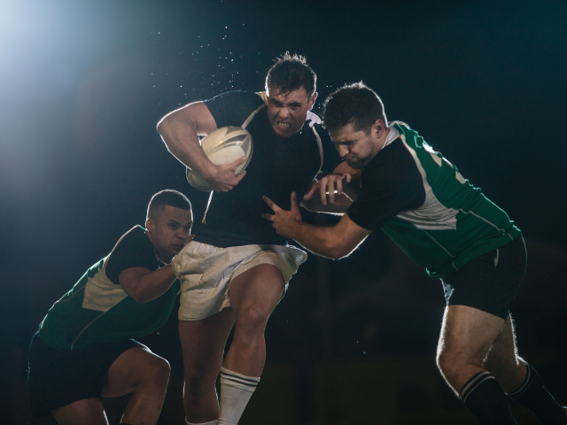 Rugby player pushing through defenders during a night match.