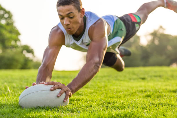 Rugby player diving to score a try on a grassy field.