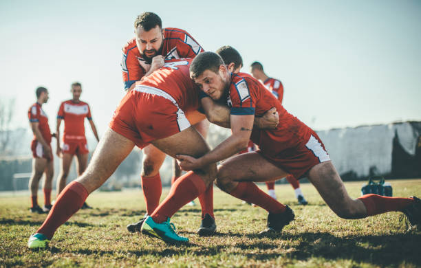 Two rugby players locking in a tackle during a daytime game, with teammates supporting the play.