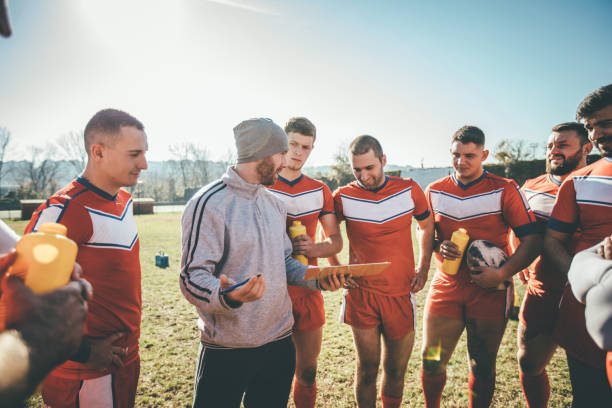 Rugby coach giving instructions to his team in bright orange jerseys.