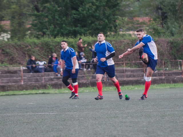 Three rugby players, one preparing to kick the ball during a match.