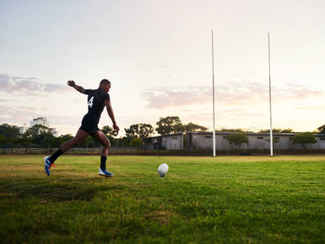 Rugby player preparing to kick the ball towards the goalposts during sunset.