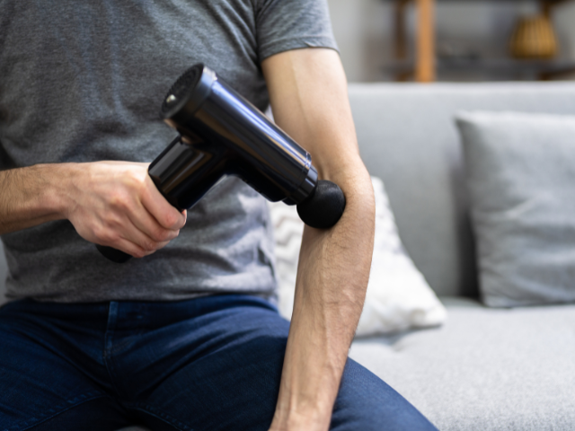 A person using a massage gun on their arm for muscle relaxation.