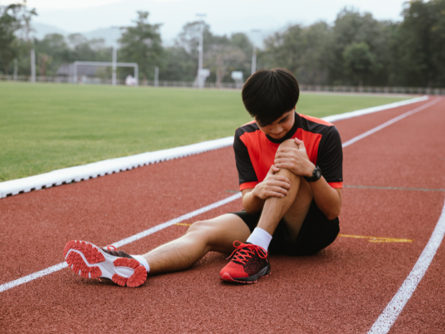 Athlete sitting on a track, holding their injured knee.