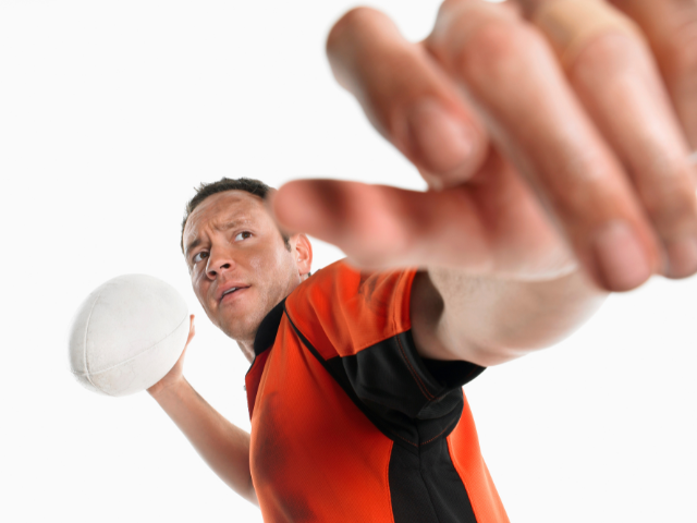 Close-up of hands gripping an American football on a grassy field.