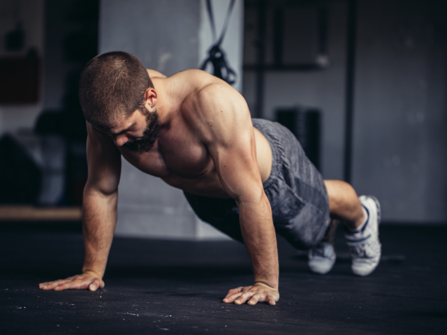 A man performing push-ups on a gym floor, shirtless, with a focused expression.