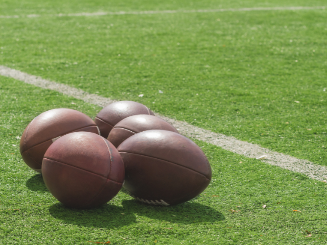 A cluster of rugby balls on a green field, ready for practice.