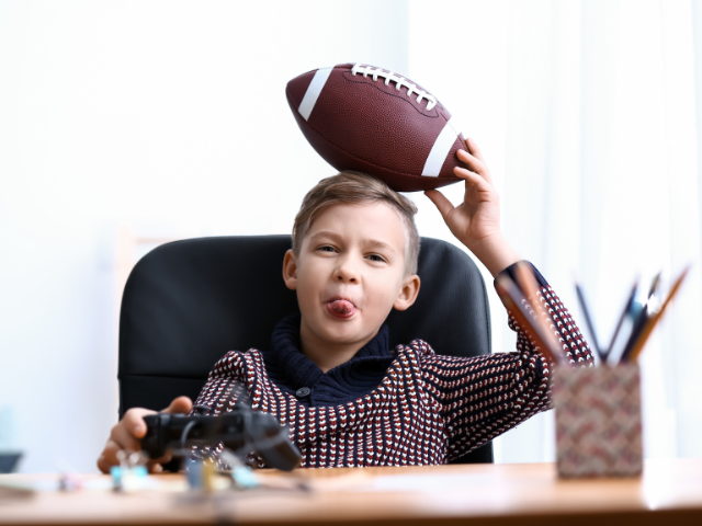  A young boy holding a rugby ball over his head and sticking out his tongue.