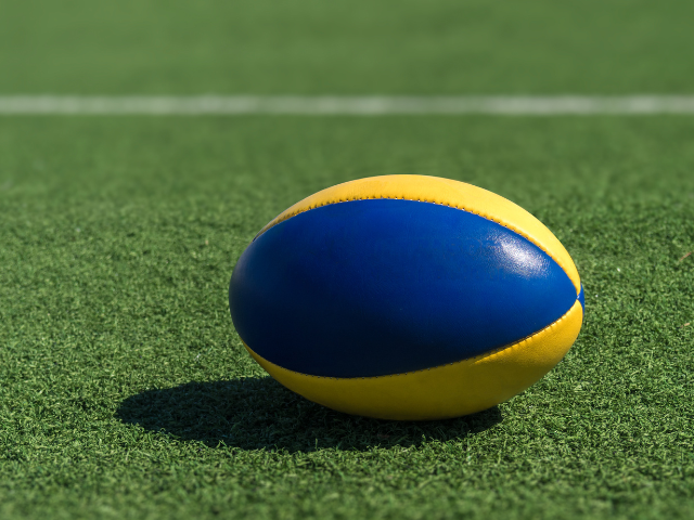 A yellow and blue rugby ball on a field of artificial grass.