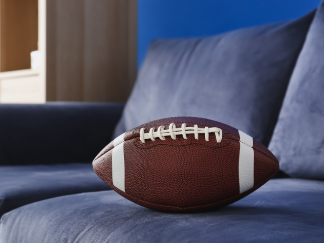 A rugby ball placed on a blue couch indoors.