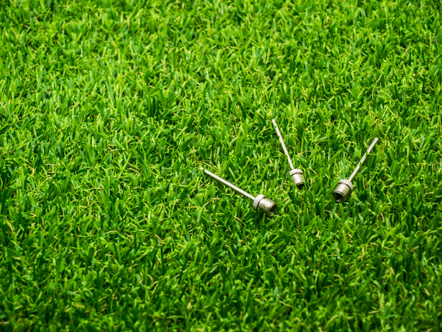 Three metal ball pump needles lying on green grass.