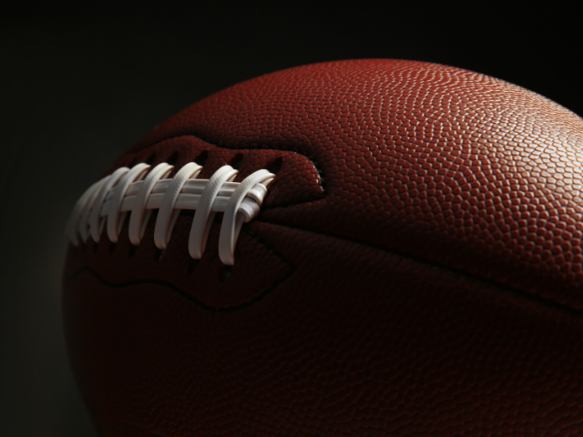  A close-up of a brown leather rugby ball sitting on green artificial turf.