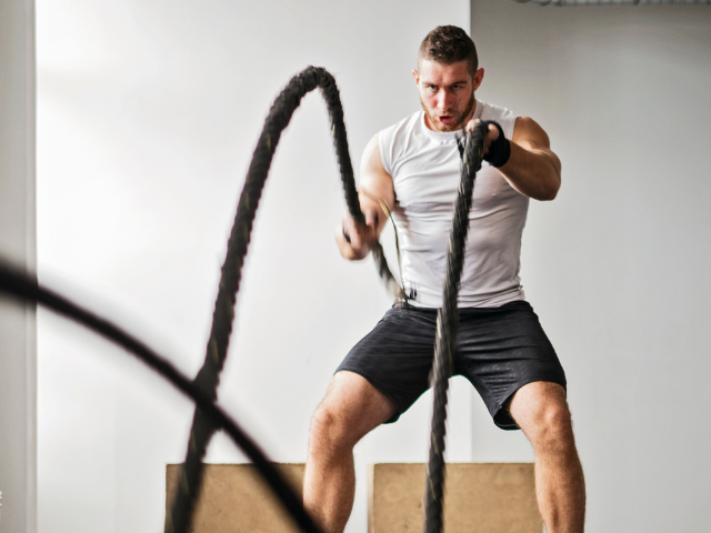 A man intensely working with battle ropes during a gym session.