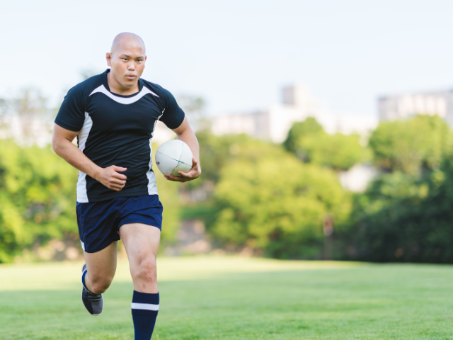 A man running with a rugby ball in hand, wearing a black and white rugby jersey