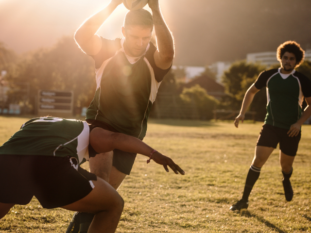  A rugby player raising the ball overhead while being tackled, with teammates in the background during a training session.