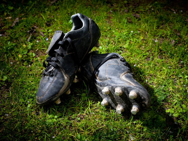 A pair of black, worn-out rugby cleats resting on grass.