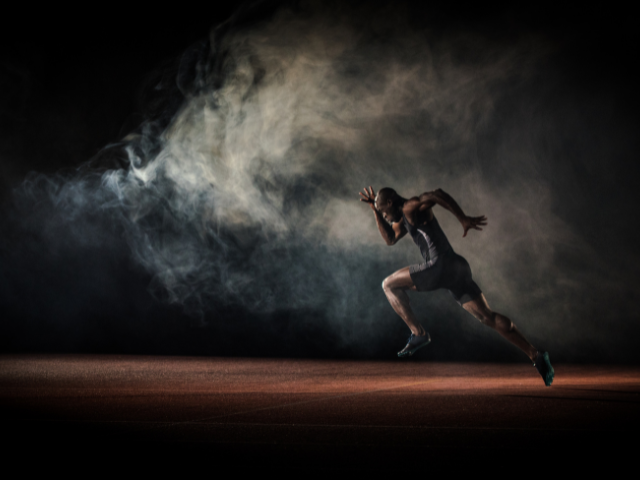 A male sprinter captured in full speed, running in a cloud of smoke against a dark backdrop.