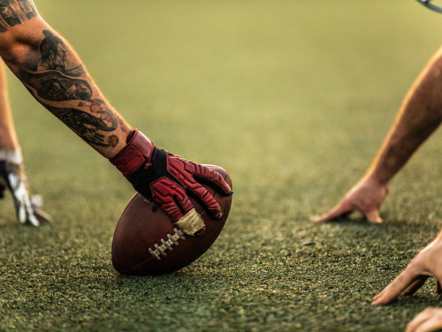 Football player wearing gloves, gripping the ball on the field before the start of play.